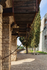 Medieval ingenuity on display with the counterweight system of a drawbridge in Brescia historic castle, framed by a stony arch and flanked by cypress trees - obrazy, fototapety, plakaty