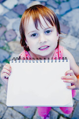 Cute little child girl holding notebook with empty copy space for text or design. Top view.
