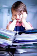 Humorous portrait of tired and exhausted business child girl working overtime alone in office with a lot of documents.