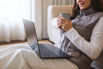 Closeup image of a young woman drinking coffee while working on laptop computer at home