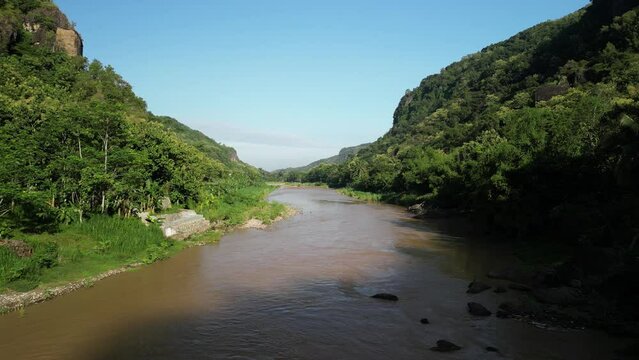 4k video Aerial view of Oya River Imogiri Jogja surrounded by Dense natural forest trees on the mountain hills with morning sunlight. Concept for International Day of Forest, World Environment Day.