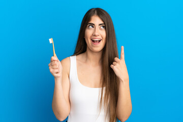 Young caucasian woman brushing teeth isolated on blue background thinking an idea pointing the...