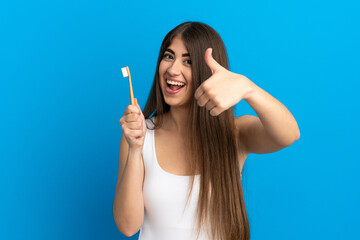 Young caucasian woman brushing teeth isolated on blue background with thumbs up because something good has happened
