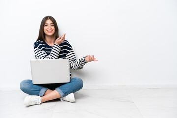 Young caucasian woman with a laptop sitting on the floor isolated on white background extending...