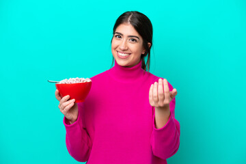 Young caucasian woman holding a bowl of cereals isolated on blue background inviting to come with...
