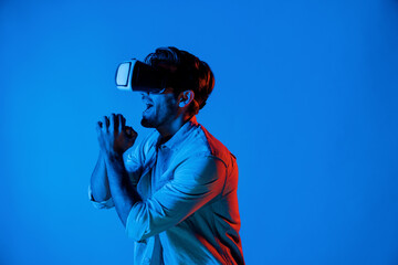 Caucasian man singing a song in virtual world at neon background by using VR goggles or technology...