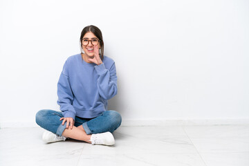 Young caucasian woman sitting on the floor isolated on white background shouting with mouth wide...