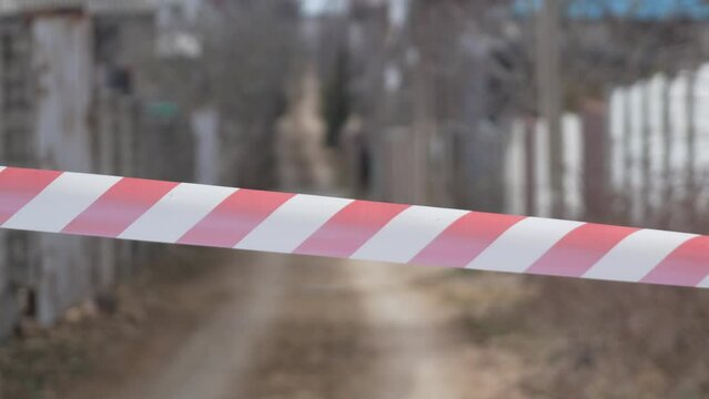 Red and white warning tape swinging in the wind. Protection sign. Don't cross the line. Red White caution tape pole fencing is protects for No entry. Backdrop without people, empty street.