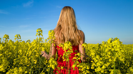 Caucasian woman in red dress in scenic yellow rapeseed field