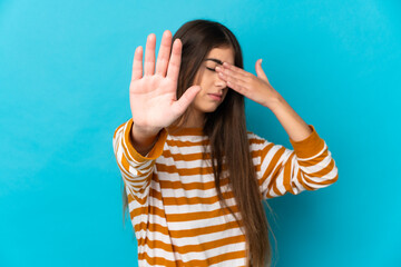 Young caucasian woman isolated on blue background making stop gesture and covering face