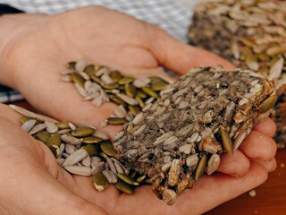 healthy bread, close-up, Lena pumpkin seeds and seeds in the palms, buckwheat bread, freshly baked, sliced, striped tablecloth, hands holding a piece of bread, heart shape