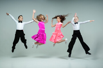 two curly-haired girls and two boys engaged in ballroom dancing laughing and mischievously jump up