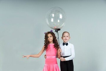 curly-haired girl and a boy engaged in ballroom dancing pose with balloons in a photo studio