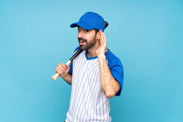 Young man playing baseball over isolated blue background listening to something by putting hand on...