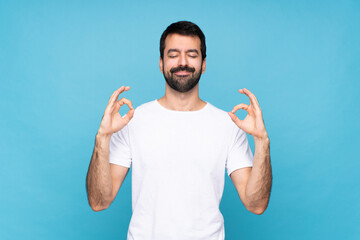 Young man with beard  over isolated blue background in zen pose