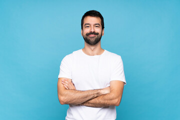 Young man with beard  over isolated blue background keeping the arms crossed in frontal position