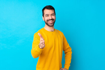 Young caucasian man over isolated blue background shaking hands for closing a good deal