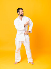 Full-length shot of man over isolated yellow background doing karate and pointing to the lateral