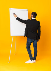 Full-length shot of businessman giving a presentation on white board over isolated yellow background