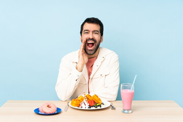 Man at a table having breakfast waffles and a milkshake shouting with mouth wide open