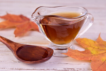 Maple syrup in a gravy boat and a maple leaf. Close-up.
