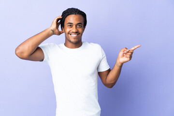 Young African American man with braids man isolated on purple background surprised and pointing...