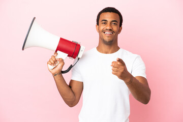 African American handsome man on isolated pink background holding a megaphone and smiling while...
