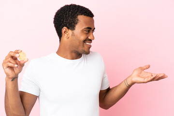 Young African American man holding a Bitcoin over isolated pink background with surprise expression...