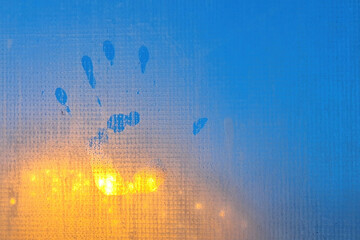 A handprint on the foggy surface of a plastic window. In the background there is the blue of the...