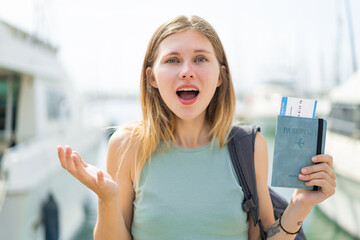 Young blonde woman holding a passport at outdoors with shocked facial expression