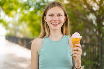Young blonde pretty woman with a cornet ice cream at outdoors smiling a lot
