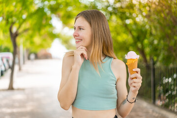 Young blonde pretty woman with a cornet ice cream at outdoors thinking an idea and looking side