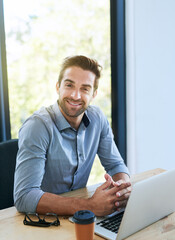 Portrait, business man and smile with laptop in desk at office in startup company as architect. Entrepreneur, table and happy for research, ideas and planning on internet for creativity or project