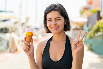 Young pretty Bulgarian woman with a cornet ice cream at outdoors smiling and showing victory sign