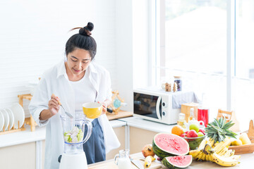 Young woman making health drink. Woman putting fruits and vegetables into the electric blender.