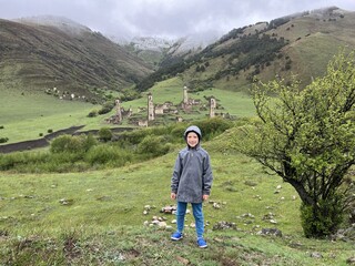 A boy in the background of the medieval Targim tower complex in the Caucasus mountains, surrounded...