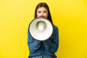 Young caucasian woman isolated on yellow background shouting through a megaphone to announce something