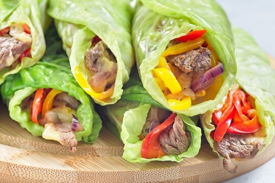 Cabbage leaves wraps with beef, vegetables and cheese, on a round wooden board, horizontal closeup