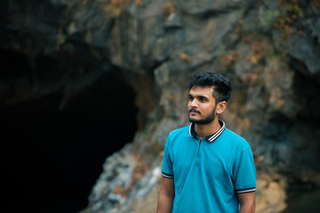 Young indian man wearing blue t-shirt standing in a cave.
