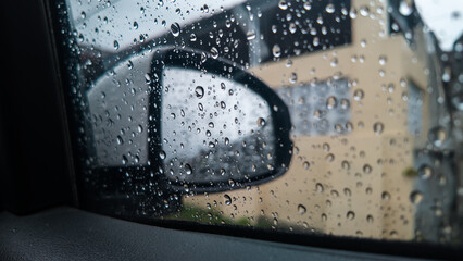 Water drops on car side window and rearview mirror while driving during rainy day.
