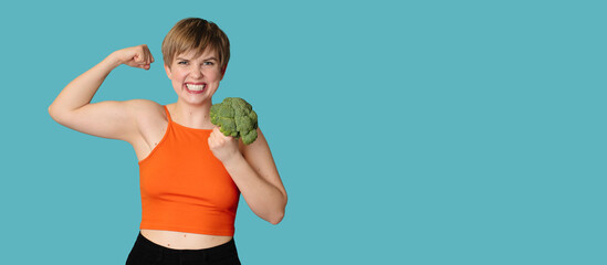 A smiling Caucasian girl with fresh broccoli in her hands as dumbbells. Panoramic banner, free...