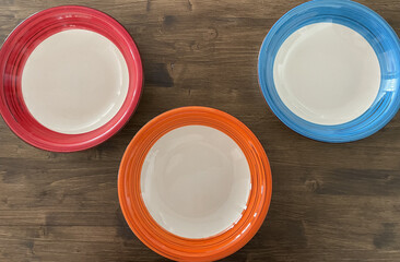 Three plates of different colors on a wooden table background
