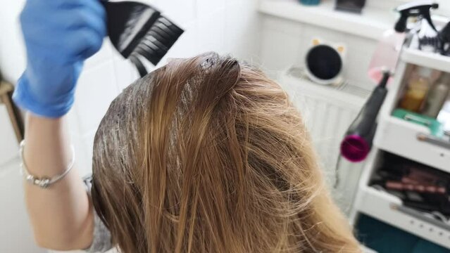 Blonde attraktive Frau, die sich Haarfarbe mit einem Pinsel auftr&auml;gt