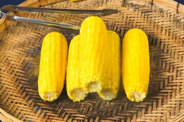 Boiled ears of corn rest on a woven bamboo tray, their bright yellow kernels offering a healthy,...
