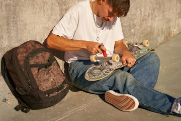 Stylish young man repairing his skateboard in the skate park. Extreme sport concept
