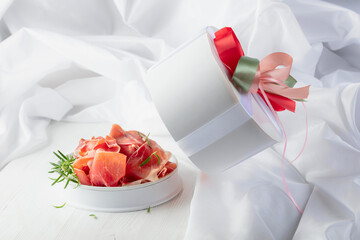 Prosciutto with rosemary in gift box on a white wooden table.