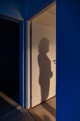 A woman's shadow in the doorway of a bedroom in an apartment.