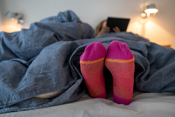 A woman's feet with socks underneath big down comforter in a bedroom.