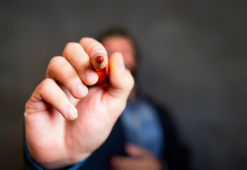 Man taps the point of a red pencil at the camera and at you. Voting pencil with red writing color. Cast a vote in the Netherlands. Focus on the sharp red point