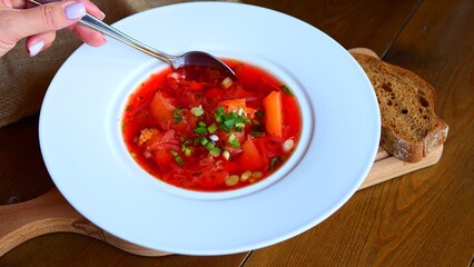 Womans hand gently stirs vibrant beetroot soup in bowl, creating mesmerizing beetroot swirls of color. The beetroot, a versatile root vegetable, infuses the soup with its distinctive earthy sweetness.